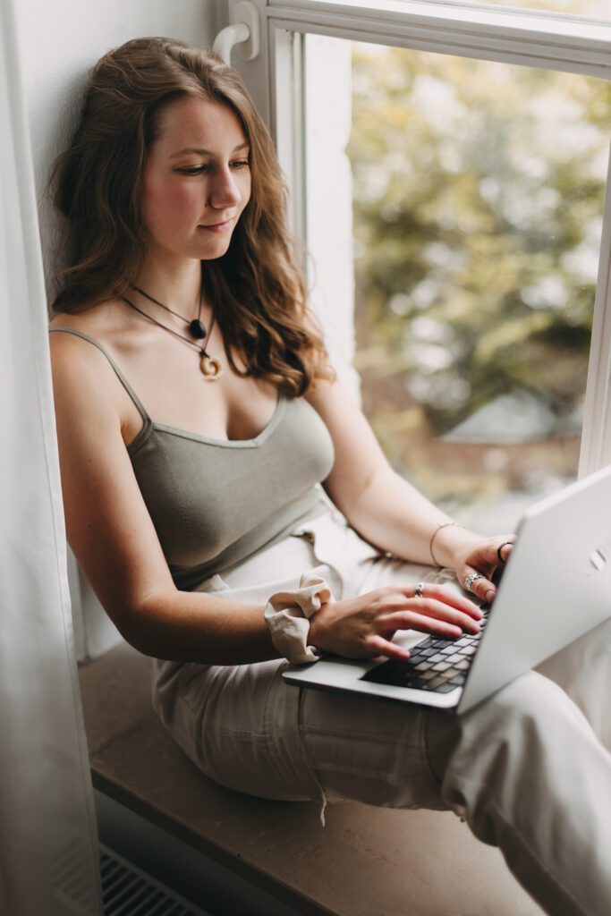 Junge Frau sitzt mit einem Laptop am Fenster
