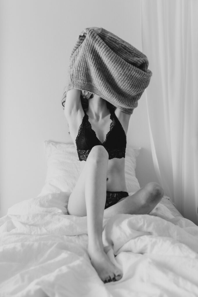 Sitzende Frau in Unterwäsche mit Pullover vor dem Gesicht