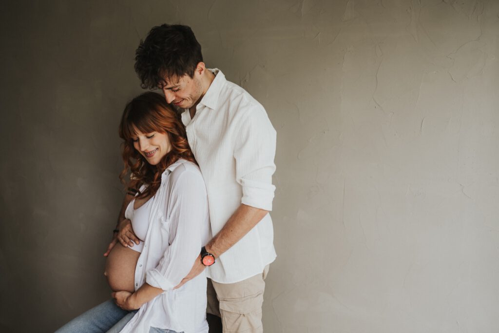 Pärchen vor einer schlichten Betonwand. Babybauch ist zu sehen