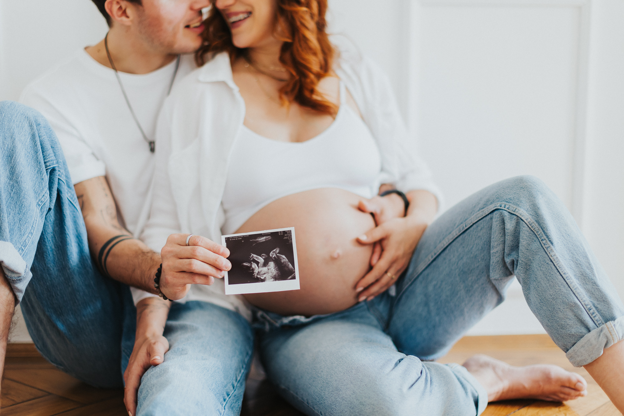 Babybauchfotos mit Ultraschallbild. Pärchen sitzt auf dem Boden